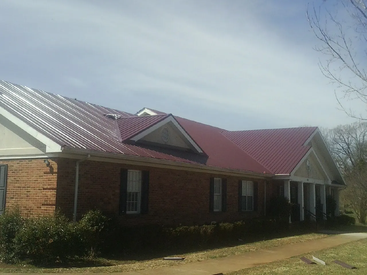Red metal roof with gabled entries on a long brick building, from a Hail Damage Roof Repair job in Antimony