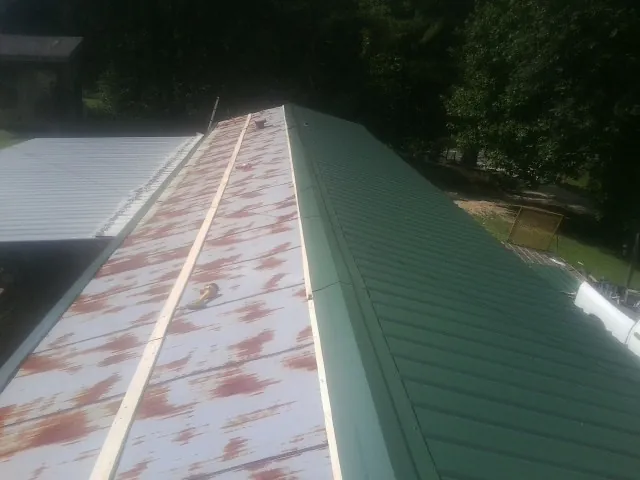 Old rusted panels beside newly installed green metal roofing — Wind Damage Roof Repair by Roofing Brothers in Antimony